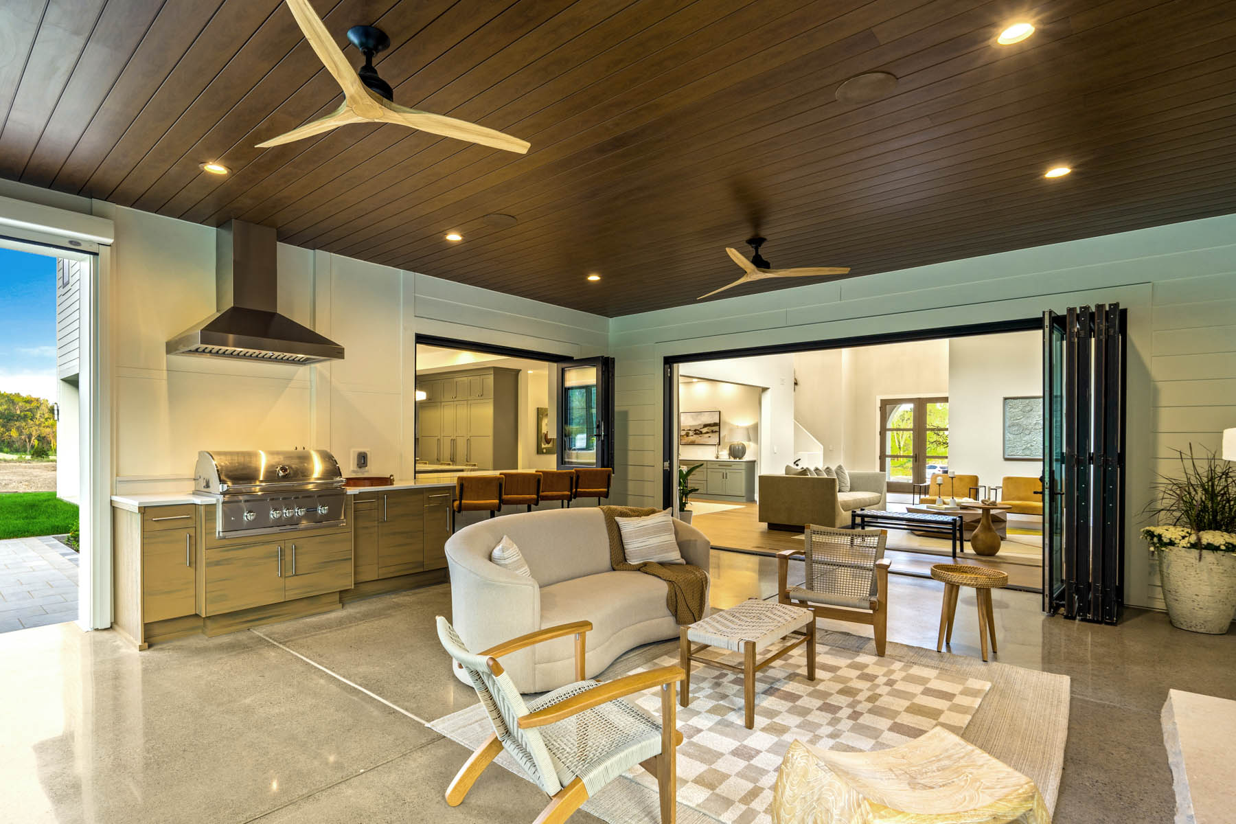 furniture, built in kitchen, bar seating and 2 way fire place of inside of three season room with accordion black framed doors between inside and outside