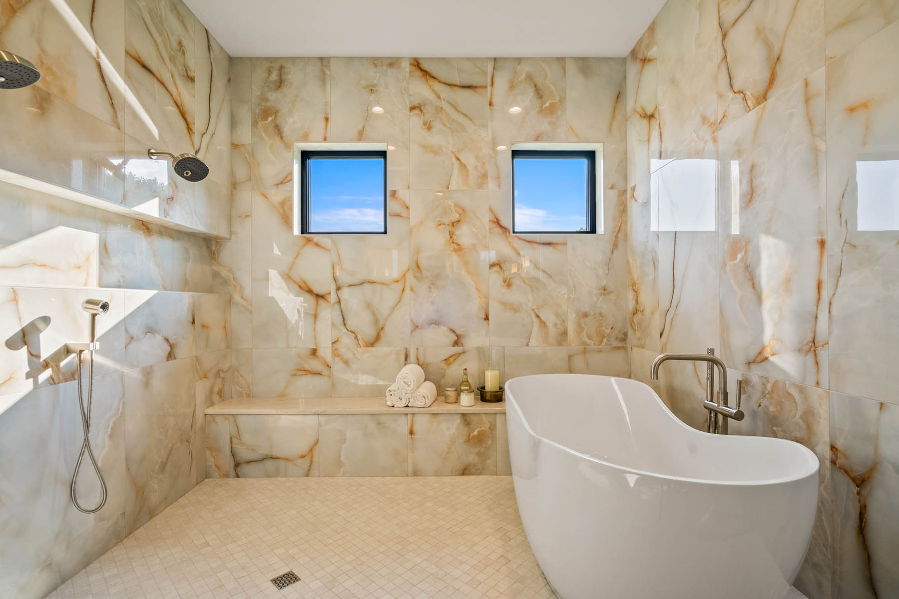primary suite wetroom with large stand alone soaking tub, tiled walls and shelf and multiple shower heads on wall