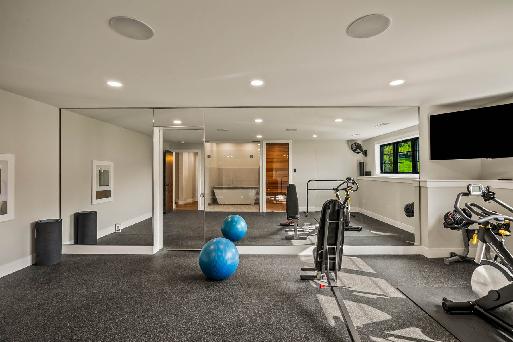 Workout room with mirrors reflecting in home sauna and cold plunge area